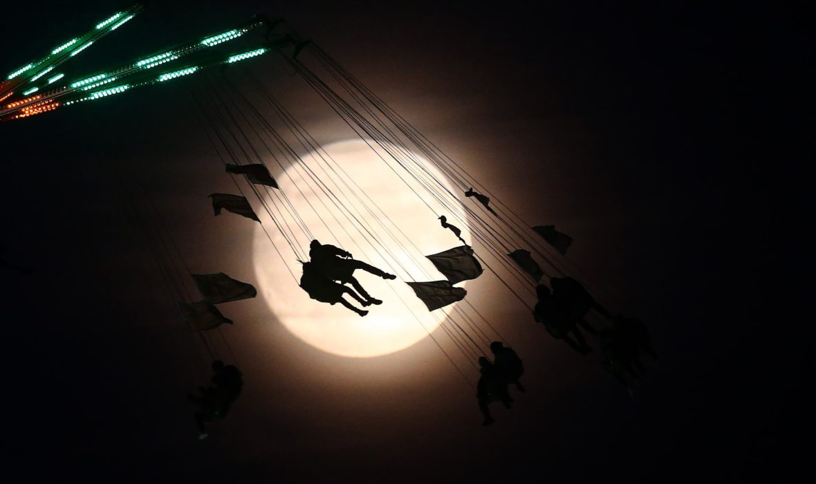 People on a funfair ride are silhouetted against the moon a day before the supermoon spectacle, in London